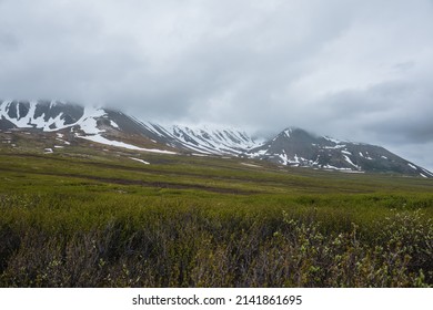 Dramatic alpine landscape with snowy mountains in gray low clouds. Bleak atmospheric scenery of tundra under lead gray sky. Gloomy minimalist view to mountain range among low rainy clouds in overcast. - Shutterstock ID 2141861695