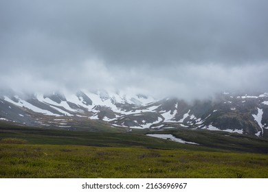 Dramatic alpine landscape with snowy mountains in gray low clouds. Bleak atmospheric scenery of tundra under lead gray sky. Gloomy minimalist view to mountain range among low rainy clouds in overcast. - Shutterstock ID 2163696967