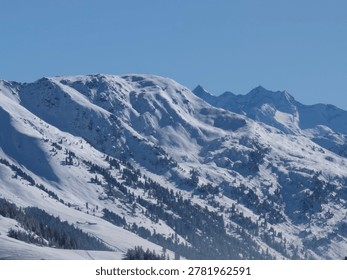 Dramatic alpine mountain range covered in snow beneath a clear blue sky.