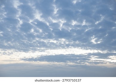 Dramatic altocumulus cloud formation spreading across the blue sky with a soft glowing horizon during evening sunset