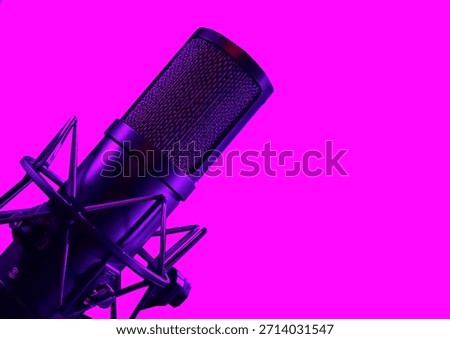 A dramatic, angled close-up of a studio microphone in a shock mount set against a stark, vibrant magenta background.