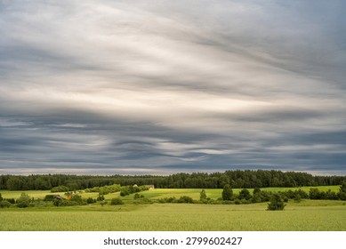 Dramatic Asperitas cloud formation creating wave-like patterns across the sky above a green rural landscape with fields, meadows and forest. Unusual atmospheric phenomenon and striking cloudscape in the countryside