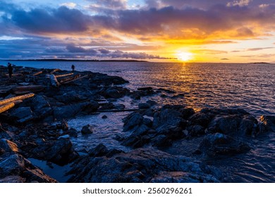 Dramatic atmospheric sunrise painting the ocean horizon and rocky shore under vibrant orange and purple hues. - Powered by Shutterstock