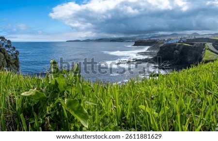 Dramatic bay of Cahetas on the north coast of São Miguel. Green landscape (Viriditas naturae) in the foreground, Rabo de Peixe behind. Changeable Azores weather with sun and clouds.