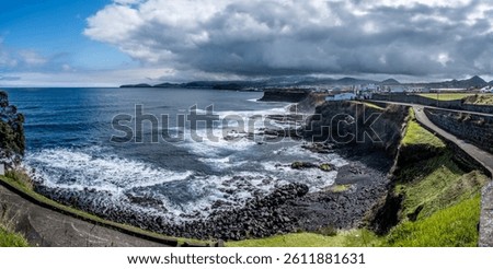 Dramatic bay of Cahetas on the north coast of São Miguel. Green landscape (Viriditas naturae) in the foreground, Rabo de Peixe behind. Changeable Azores weather with sun and clouds.