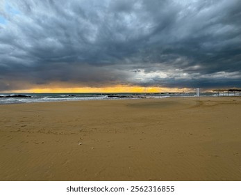 A dramatic beachscape with golden sunlight piercing through stormy clouds at sunset, illuminating the sandy shore and restless waves, creating a captivating blend of tranquility and intensity