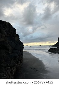 Dramatic black volcanic cliffs frame moody seascape at sunset. Dark volcanic beach with crashing waves. Rugged coastline with stormy clouds and golden horizon. Benijo beach, Tenerife. 