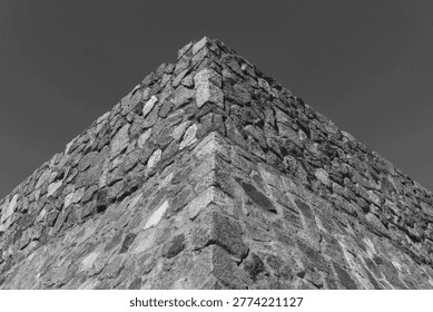 Dramatic black and white architectural perspective of a solid masonry building corner. The textured granite rocks create a powerful sense of strength, stability, and historical endurance. Minimalist composition with high contrast and sharp edges