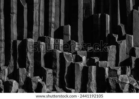 Dramatic black and white background capturing the stark geometry of towering basalt column formations at Black Sand Beach, Vik in Iceland