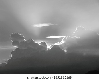 Dramatic black and white capture of sunrays piercing through dark, voluminous clouds, highlighting their edges.