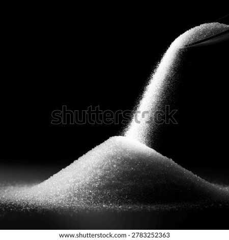 A dramatic black and white close-up of sugar being poured from a spoon onto a mound of sugar, creating a dynamic flow.