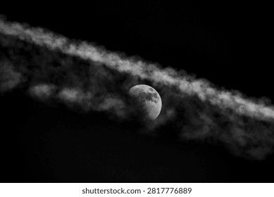 A dramatic black and white image captures the moon peeking through a long, textured cloud formation, creating a sense of mystery and wonder