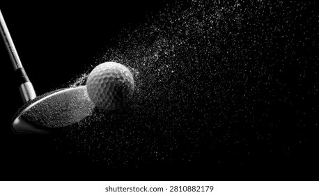 A dramatic black and white image capturing the precise moment a golf club strikes a golf ball, with a spray of dimples and dust exploding outwards.