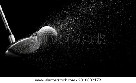 A dramatic black and white image capturing the precise moment a golf club strikes a golf ball, with a spray of dimples and dust exploding outwards.