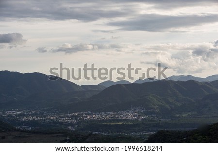 Dramatic black and white image of Caribbean mountains at sunset with the lights of the small Caribbean town of Ocoa in the foreground.