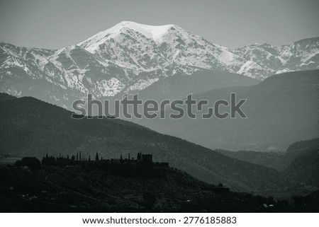 Dramatic black and white landscape of the snow-capped Atlas Mountains towering over a remote hillside village in Morocco