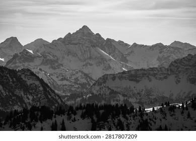 Dramatic black and white panoramic view of rugged snow-covered mountain peaks and ridges in the Alps