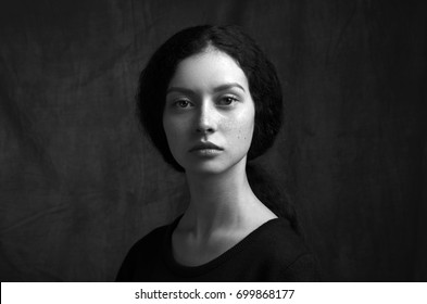 Dramatic black and white portrait of a beautiful lonely girl with freckles isolated on a dark background in studio shot
