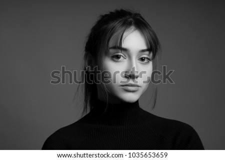 Dramatic black and white portrait of a beautiful lonely girl with freckles isolated on a dark background in studio shot.