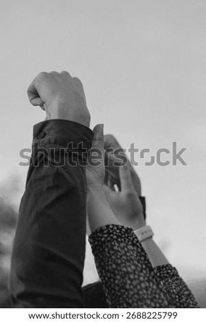 Dramatic black and white shot of multiple hands raised toward the sky in a gesture of hope, unity, or protest. Low angle view highlighting arms reaching up against a clear sky.