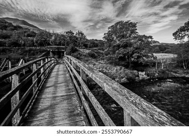 Dramatic Black and White view along a weathered Wooden Hiking bridge crossing the river Glaslyn in Eryri National Park in Wales. - Powered by Shutterstock