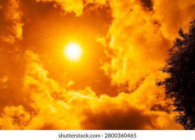 Dramatic blazing sun shining through fiery orange clouds during an extreme heatwave, global boiling and climate crisis concept, hot summer weather background.