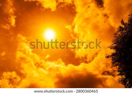 Dramatic blazing sun shining through fiery orange clouds during an extreme heatwave, global boiling and climate crisis concept, hot summer weather background.