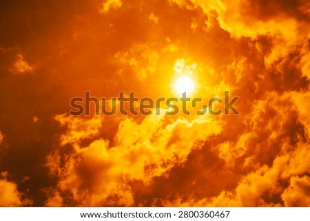 Dramatic blazing sun shining through fiery orange clouds during an extreme heatwave, global boiling and climate crisis concept, hot summer weather background.