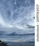 Dramatic blue and gray cloudy sky with cirrus and cumuls formation. Bird silhouette flying alone, symbolizing freedom and vastness.