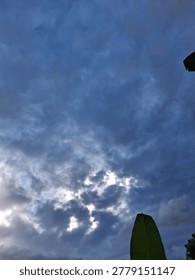 Dramatic blue and grey clouds fill the sky during a gloomy afternoon with sunlight peeking through the overcast layer above green