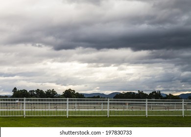 Dramatic blue and grey fractus storm clouds at sunset over an empty Australian horse race course with trees and mountains in the distance