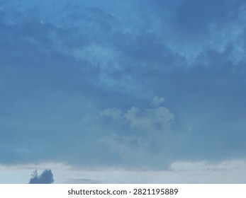 A dramatic blue hour sky captured during twilight, featuring a deep indigo backdrop layered with thick, dark clouds. The heavy cloud cover appears dense and sombre, creating a strong contrast against the cool blue tones of the fading daylight. This atmospheric scene is characteristic of the evening transition known as the “blue hour,” offering a moody and cinematic skyline.