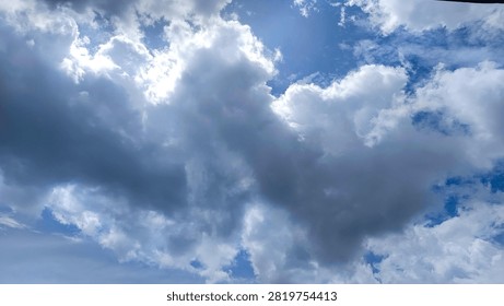 Dramatic blue sky background with thick dark clouds and bright sunlight breaking through the atmosphere.