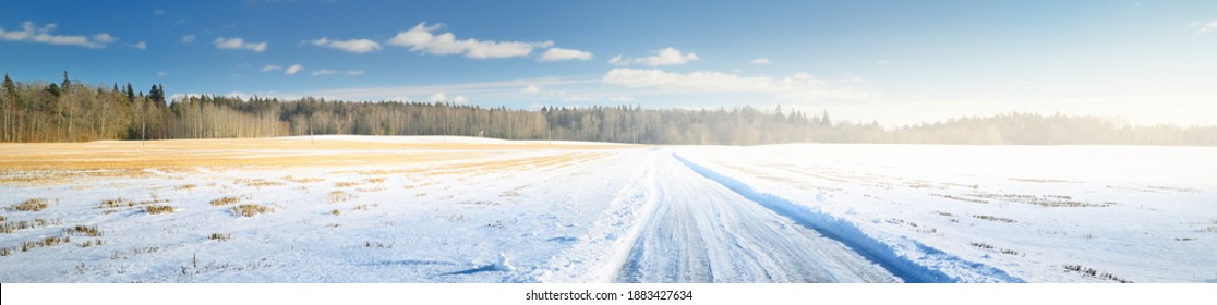 Dramatic blue sky with cumulus clouds above the snow-covered country road, agricultural field  and forest after a blizzard. Winter rural landscape. Climate change, global warming theme. Panoramic view