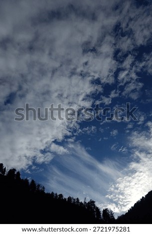 Dramatic blue sky filled with textured clouds above a dark forested mountain valley. Natural outdoor landscape with copy space, suitable for nature, weather, travel, and background concepts.