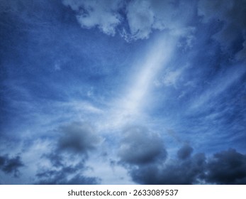 Dramatic blue sky with scattered clouds and light rays. Natural weather scene showing contrast between dark clouds and bright sky. Ideal for backgrounds and atmospheric concepts.