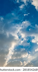 Dramatic blue sky with soft white clouds and
rays of sunlight breaking through the clouds,
creating a natural atmospheric background with
bright highlights and layered cloud formations.