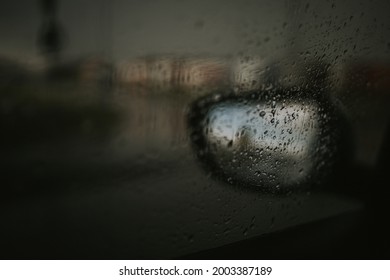 A dramatic blurred shot of the side mirror of a car seen through a window covered by raindrops