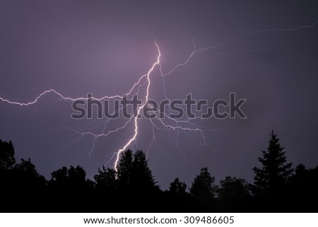 A dramatic bolt of branching lightning silhouettes foreground trees.