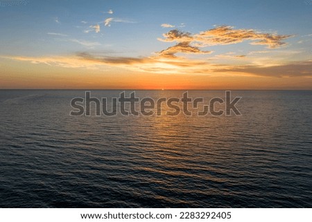 Dramatic bright red sky at ocean sunset, soft evening clouds over sea dark water