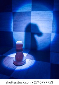 A dramatic chess scene captured in a cool blue tone, featuring a single pawn illuminated under a focused spotlight. The strong contrast casts a knight-shaped shadow on the chessboard wall, symbolizing hidden potential, ambition, and the psychological tension between identity and perception.