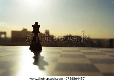 A dramatic cinematic shot captures a lone chess king piece in silhouette against a blurred city skyline during sunrise. The shallow depth of field and warm lighting create a contemplative mood, suggesting themes of strategy and leadership.
