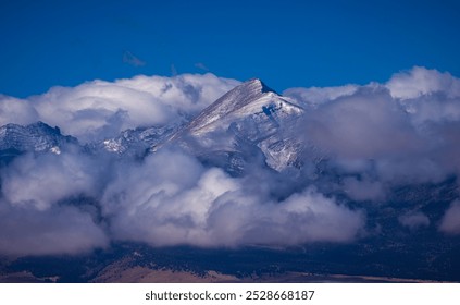 Dramatic clearing winter storm clouds surrounding a snow covered Rocky Mountain peak on a cold winter morning  - Powered by Shutterstock