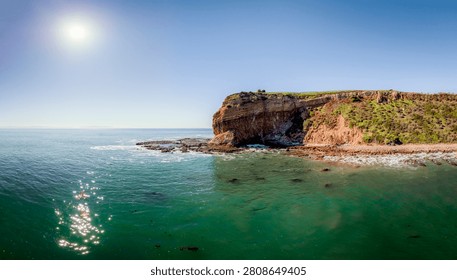 Dramatic cliffs covered in green vegetation overlook the clear turquoise waters of the Pacific Ocean under a bright sun