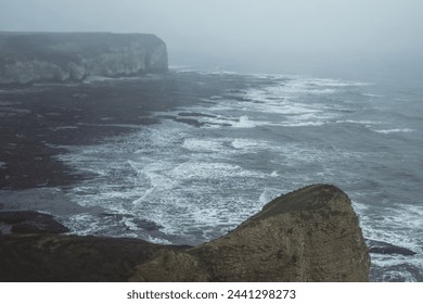 Dramatic cliffs at Flamborough Head on the east coast of Yorkshire in England on a moody, misty day.

Views over the north sea, with waves and rocks.