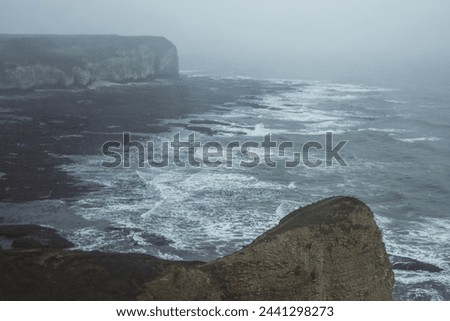 Dramatic cliffs at Flamborough Head on the east coast of Yorkshire in England on a moody, misty day.

Views over the north sea, with waves and rocks.