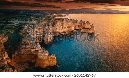 Dramatic cliffs at Ponta da Piedade, Algarve, Portugal, glowing in the golden hues of sunset. The Atlantic Ocean reflects vibrant colors, creating a breathtaking coastal view perfect for travel photog