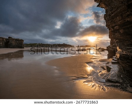 Dramatic cliffs and sandy shore of Playa de las Catedrales in Galicia, Spain, at sunset with golden light breaking through clouds, capturing natural beauty, solitude, and wonder