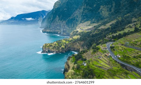 Dramatic cliffs, a winding coastal road, and terraced fields meet the Atlantic in lush Madeira. A stunning waterfall plunges into the sea.