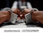 Dramatic close up of Black man wearing handcuffs on hands, criminal suspect